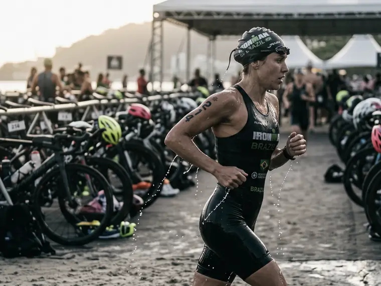 Triatleta saindo da água ainda molhada e correndo pela área de transição, entre as bicicletas no suporte